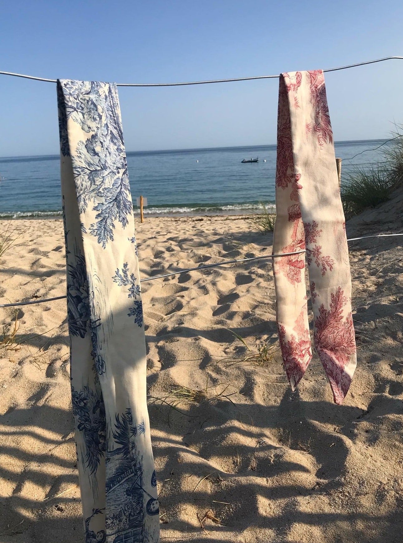 BAZAR Atelier Sablon: Foulards Jouy de Fruits en toile de Jouy rouges et bleus étendus sur une corde au bord de la mer